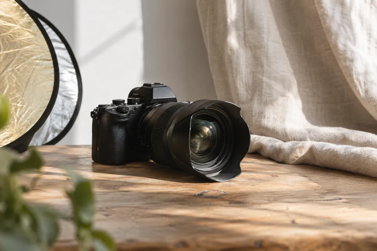 A clean professional unbranded camera and lens on a studio table beside a folded reflector and a neutral linen backdrop, close editorial crop, soft daylight — AI-generated fictional concept